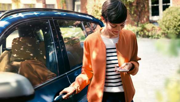 BMW Teleservices BMW Teleservices femme avec smartphone devant la porte de sa BMW