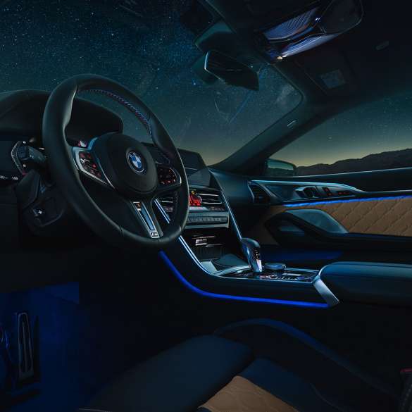 BMW M8 Competition Coupé, poste de conduite. BMW M8 Competition Coupé, prise de vue nocturne du poste de conduite avec volant M en cuir et éclairage d’ambiance bleu.