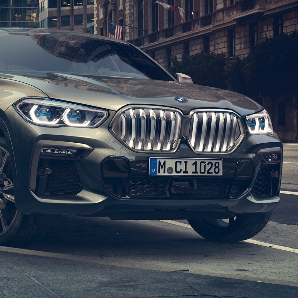 BMW X6 M50i à l’arrêt La BMW X6 M50i vue de trois quarts avant, à l’arrêt devant un décor urbain