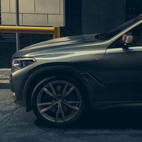 BMW X6 M50i vue de profil Homme appuyé contre la BMW X6 M50i vue de profil devant un décor urbain