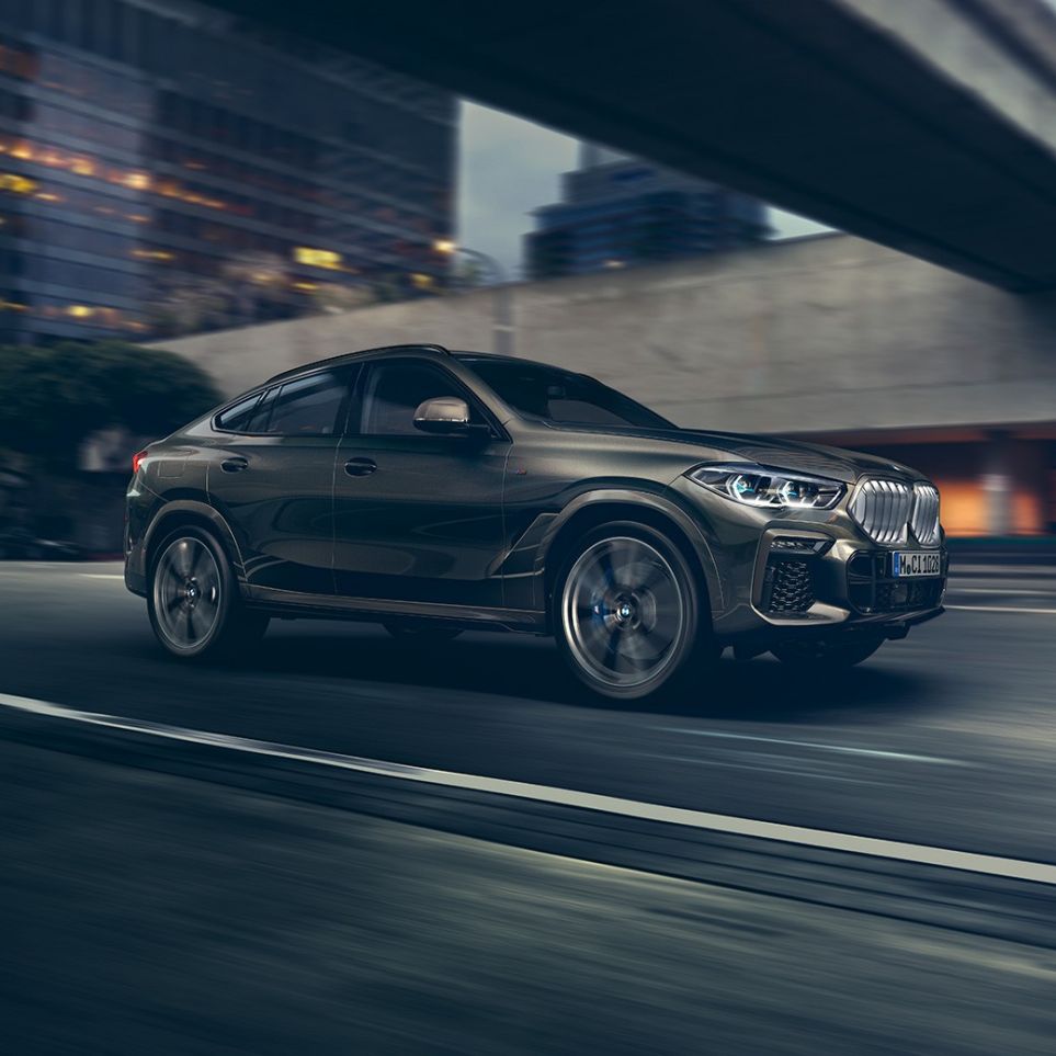 BMW X6 driving. La BMW X6 vue de trois quarts avant en marche devant un décor urbain.