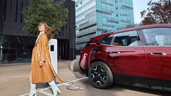 Solutions de recharge BMW pour les employeurs Solutions de recharge pour les employeurs – femme devant une BMW iX à une station de recharge
