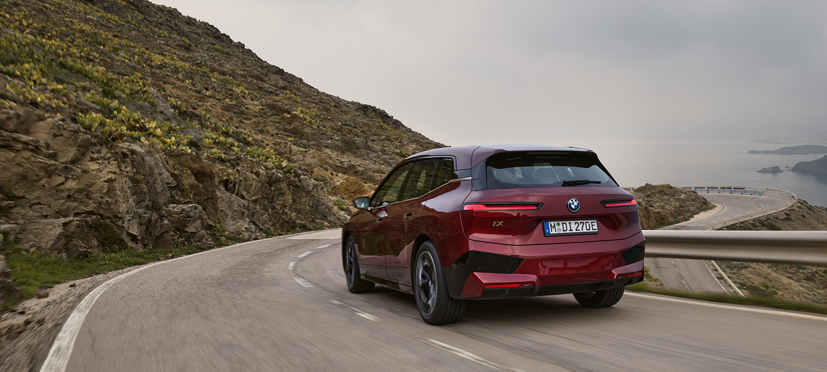 BMW iX i20 2021 SUV électrique BMW iX xDrive50 roulant sur une route côtière BMW iX i20 2021 SUV électrique BMW iX xDrive50 Aventurinrot vue arrière en roulant sur une route côtière