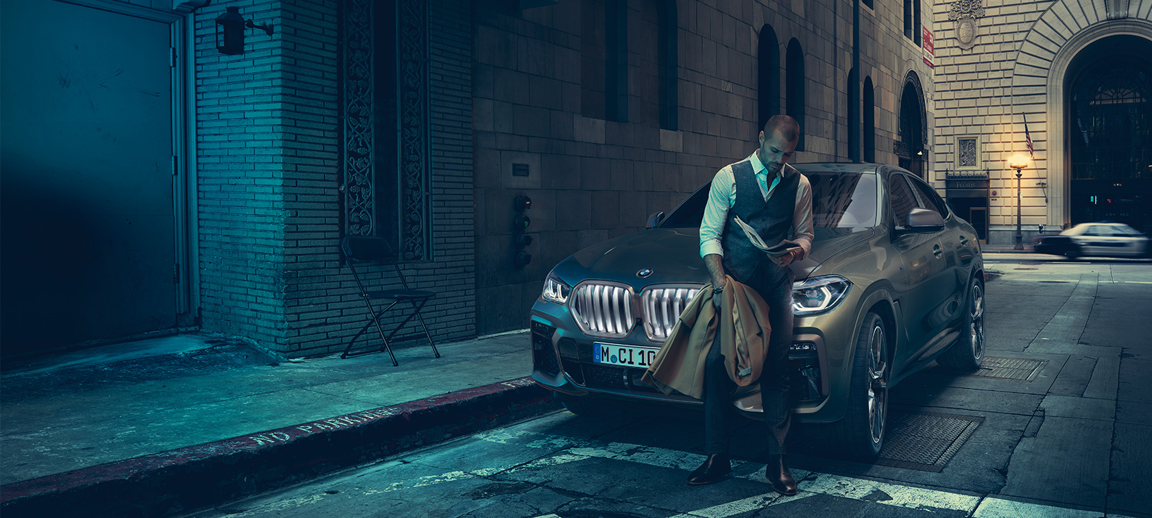 Avant de la BMW X6 M50i. Homme en appui sur l’avant de la BMW X6 M50i.