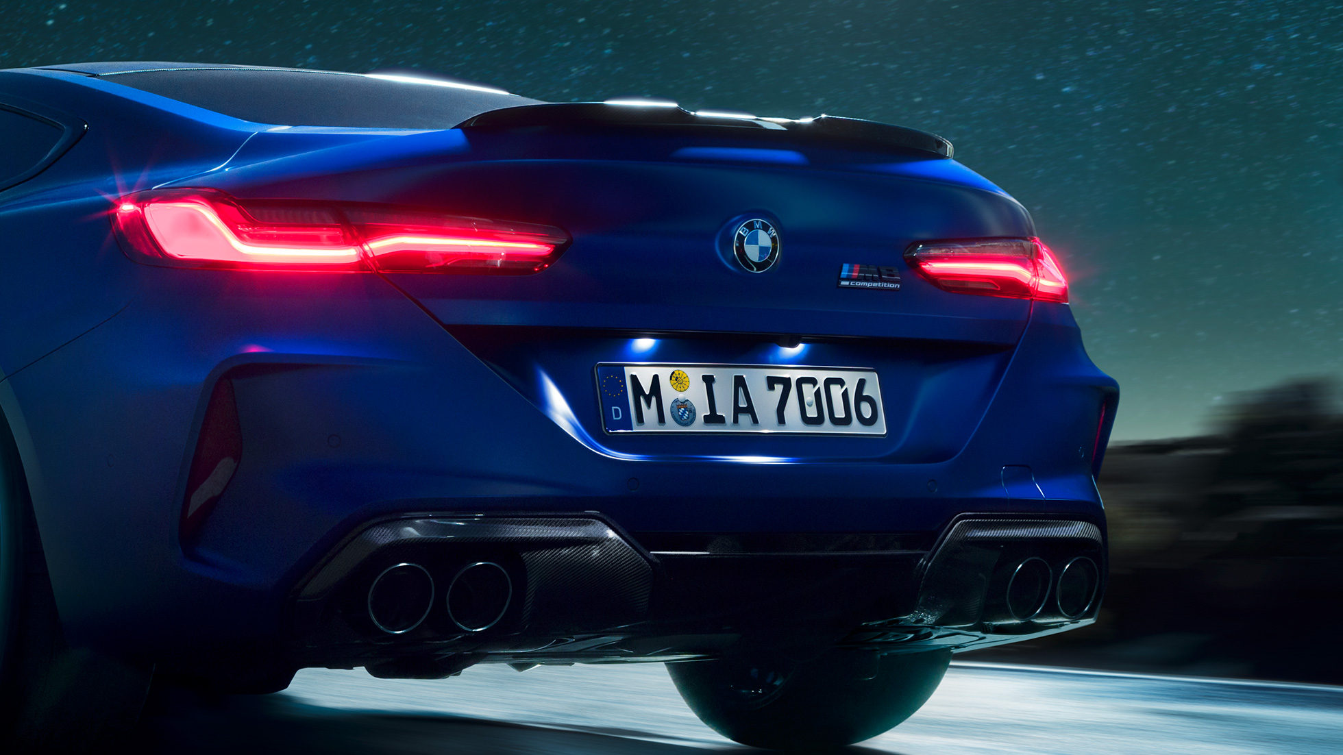 Diffuseur M en Carbon Schwarz. BMW M8 Competition Coupé en Marina Bay Blau metallic, vue en gros plan de la poupe de nuit, avec diffuseur M en Carbon Schwarz.