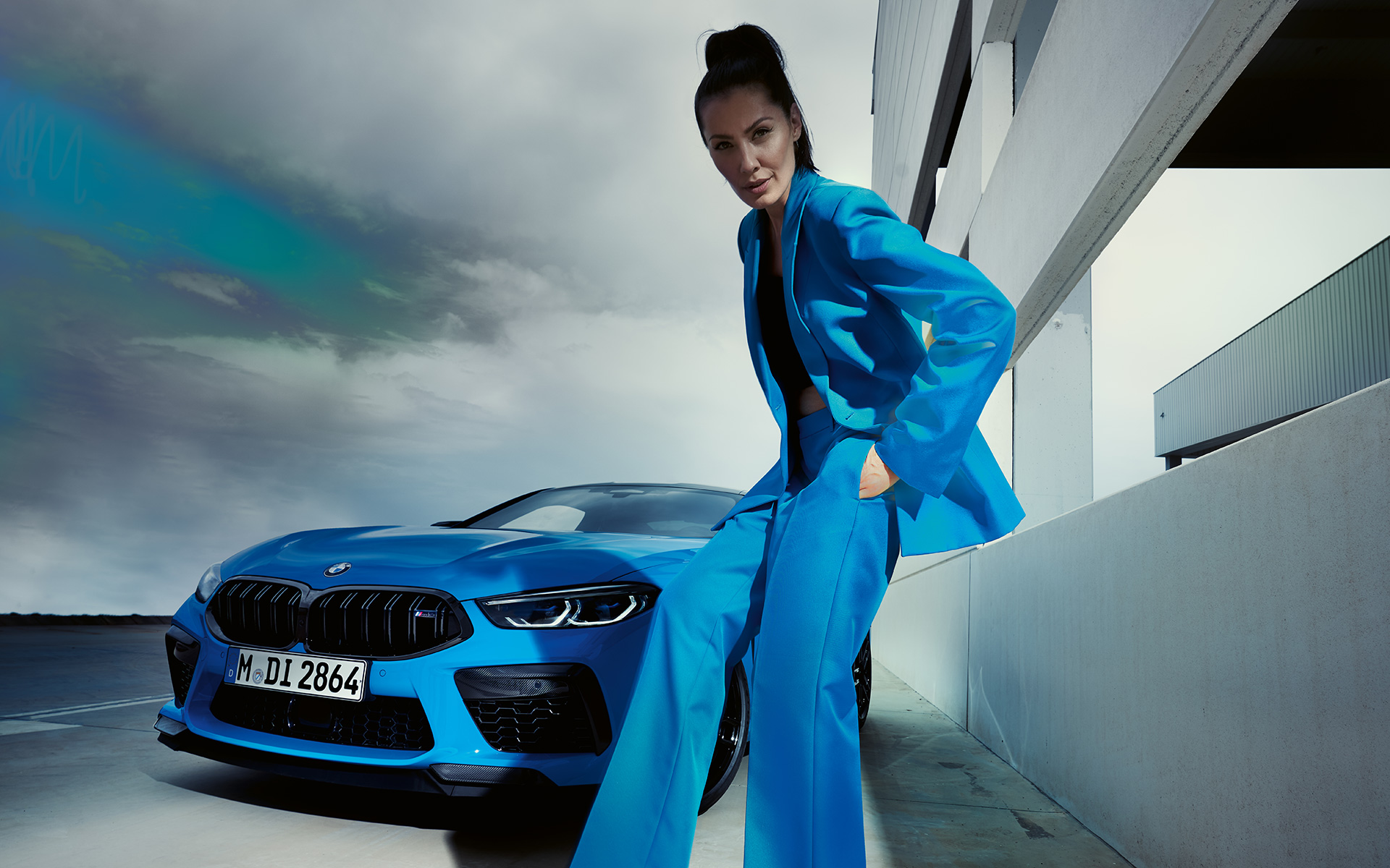 La BMW M8 Competition Coupé F92 LCI restylage 2022 Daytona Beach Blau uni vue de trois quarts avant avec mannequin femme en costume bleu