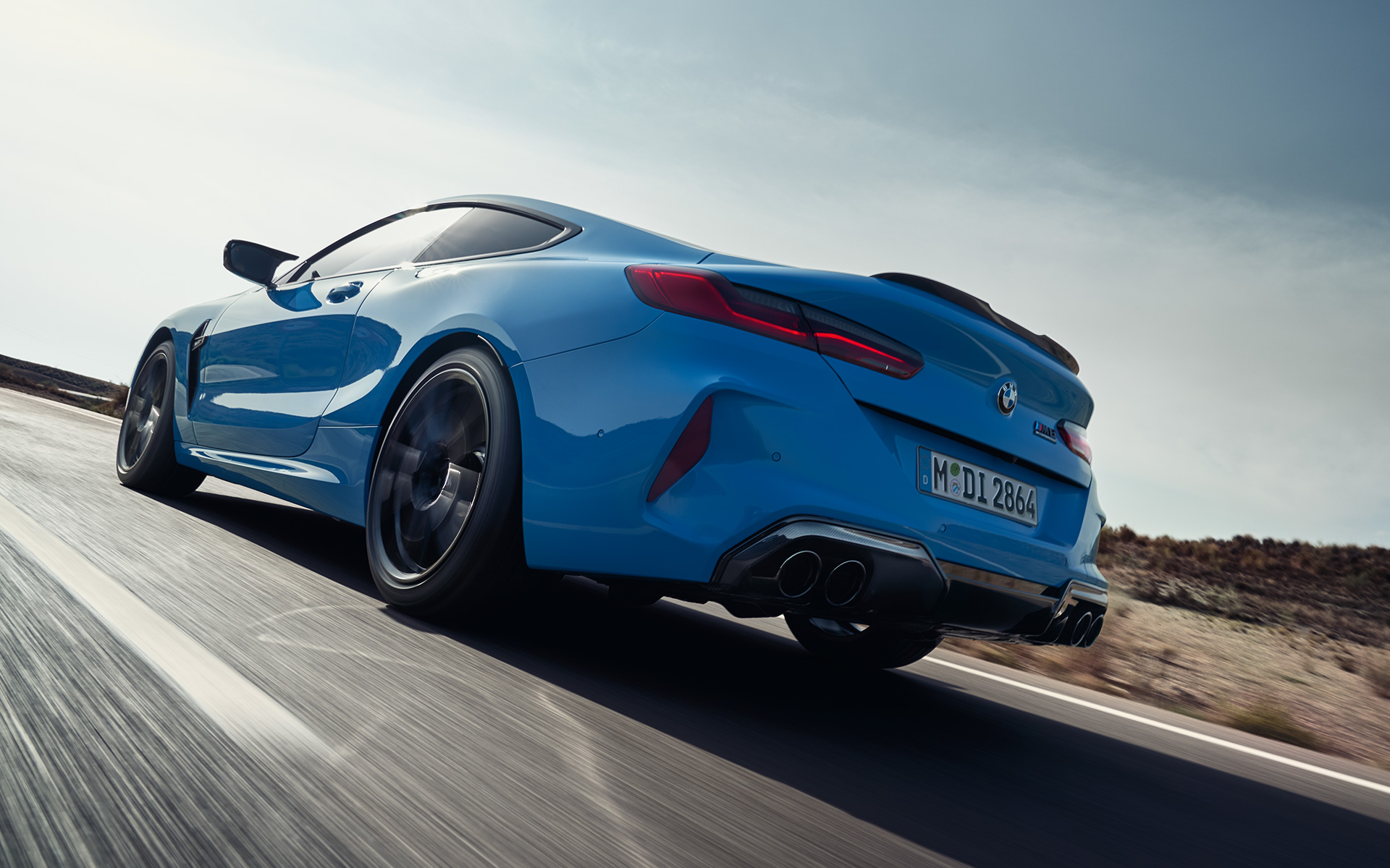La BMW M8 Competition Coupé F92 LCI restylage 2022 Daytona Beach Blau uni vue de trois quarts arrière en mouvement sur une route de campagne
