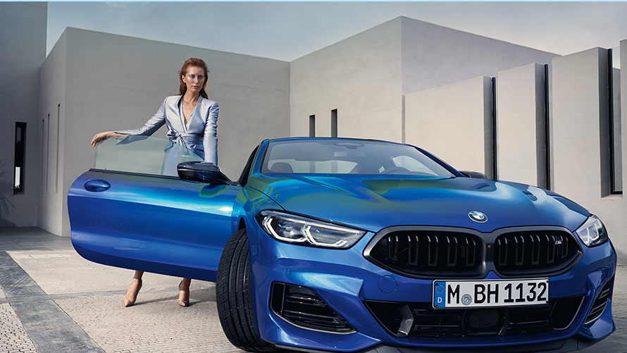 La BMW M850i xDrive Coupé G15 LCI Facelift 2022 M Portimao Blau metallic vue de face avec modèle féminin devant la portière passager avant ouverte