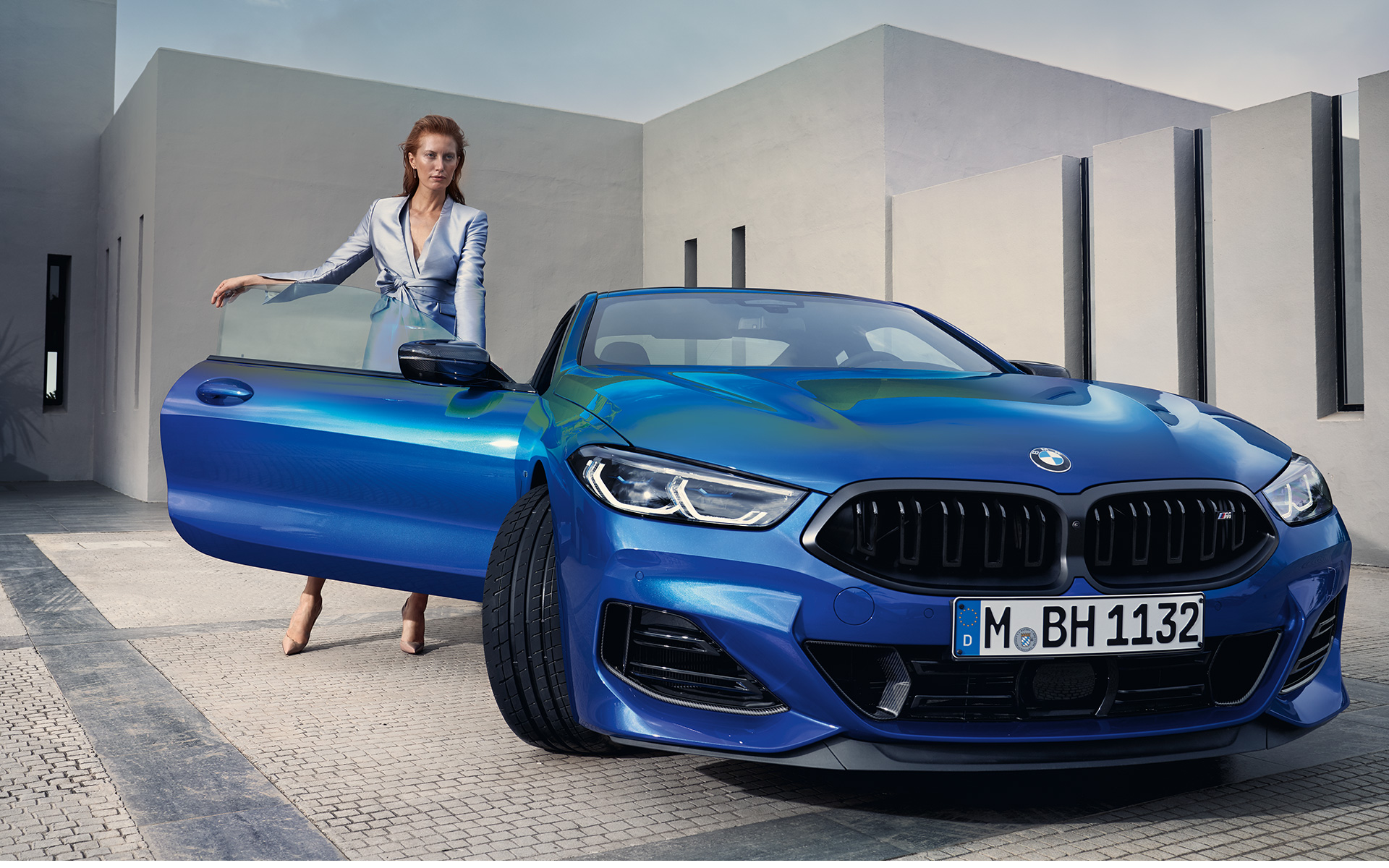 La BMW M850i xDrive Coupé G15 LCI Facelift 2022 M Portimao Blau metallic vue de face avec modèle féminin devant la portière passager avant ouverte