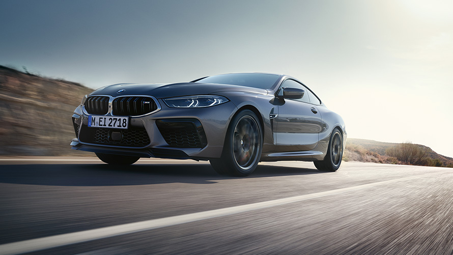 BMW M8 Coupé F92 LCI Facelift 2022 Gratte-ciel gris métallisé vue de trois quarts avant roulant sur une autoroute en contre-plongée