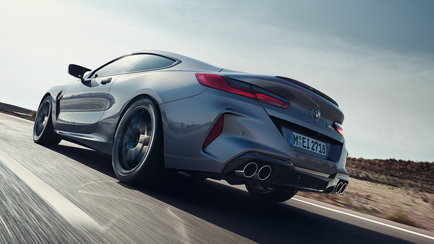 BMW M8 coupé F92 LCI lifting 2022 Gratte-ciel gris métallisé vue arrière de trois quarts roulant sur une autoroute en contre-plongée