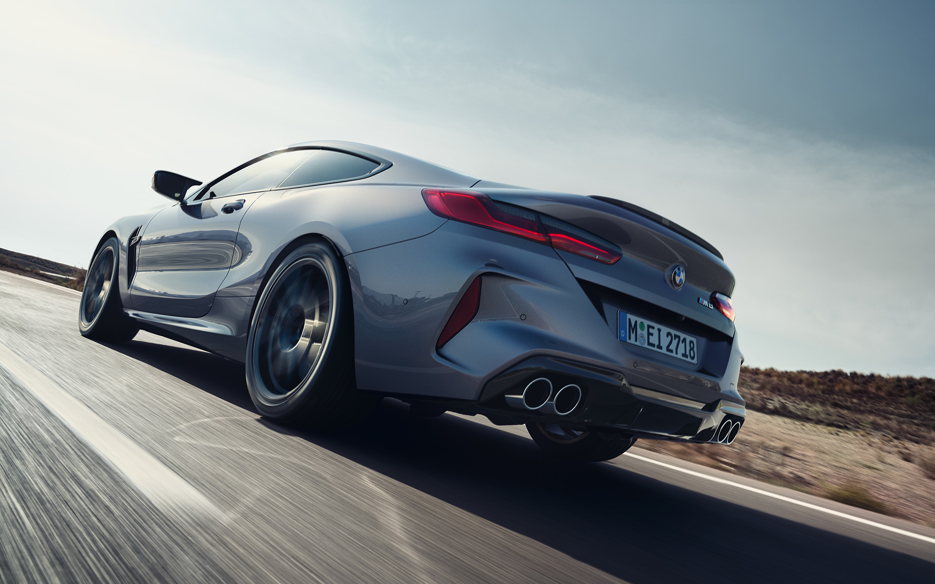 BMW M8 coupé F92 LCI lifting 2022 Gratte-ciel gris métallisé vue arrière de trois quarts roulant sur une autoroute en contre-plongée
