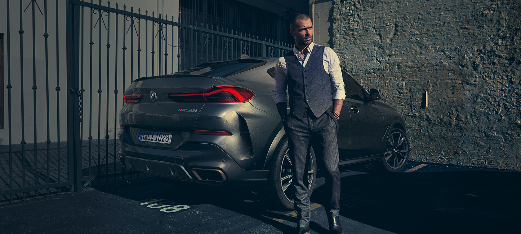 BMW X6 M50i vue de trois quarts arrière. Homme debout à côté d’une BMW X6 M50i vue de trois quarts arrière.