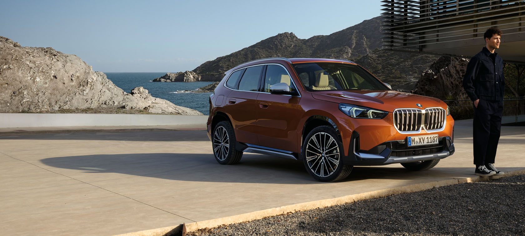 BMW X1 U11 xLine Utah orange metallic, vue de trois quarts avant sur route de campagne